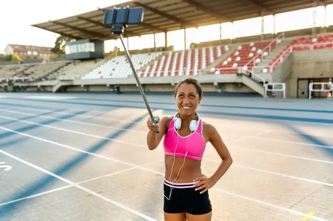 Female athlete taking selfies in stadium, holding selfie stick