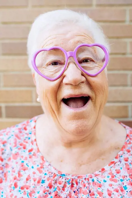 Portrait of happy senior woman wearing heart-shaped glasses pulling funny faces