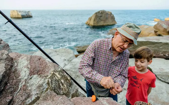 Grandfather teaching grandson fishing at the sea