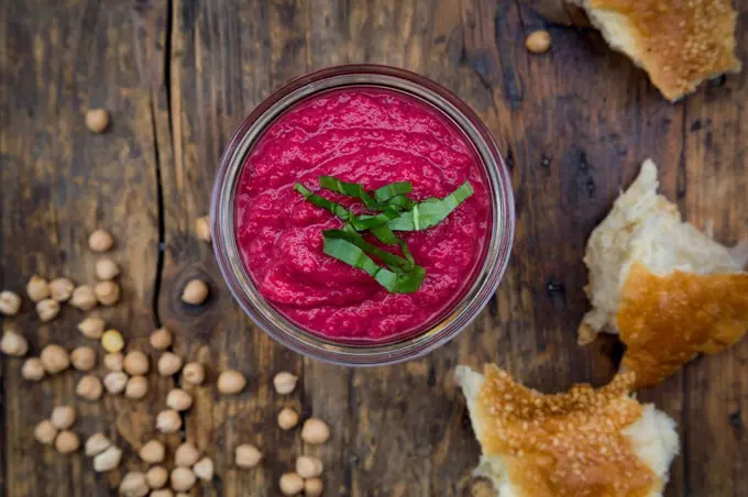 Glass of beetroot hummus, chick-peas and flat bread on dark wood