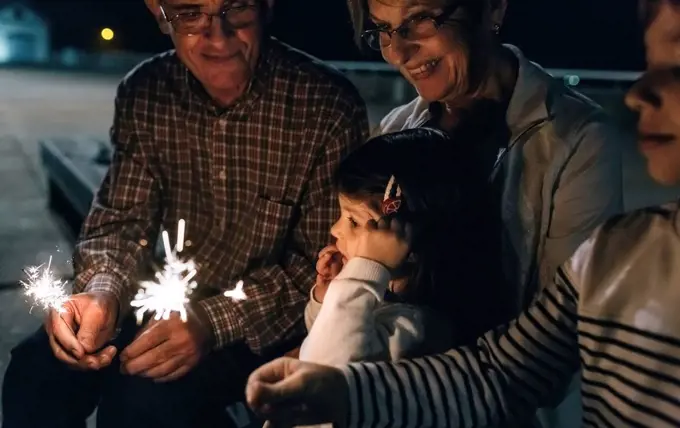 Grandparents with grandchildren holding sparklers at night