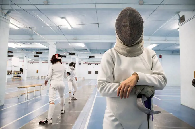 Female fencer wearing fencing mask with fencing match in the background