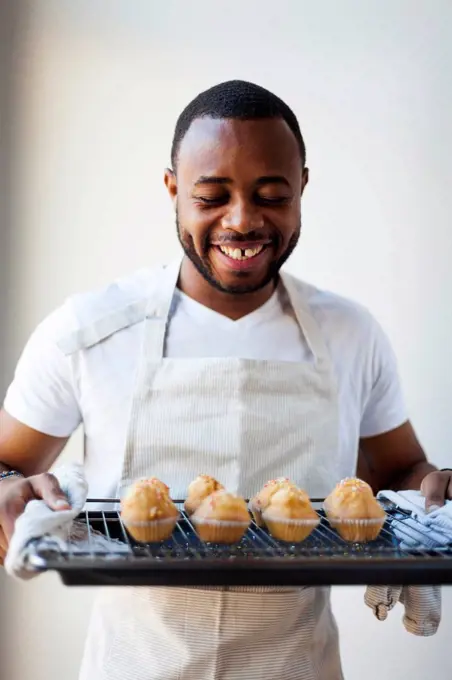 Happy young man holding tray with muffins