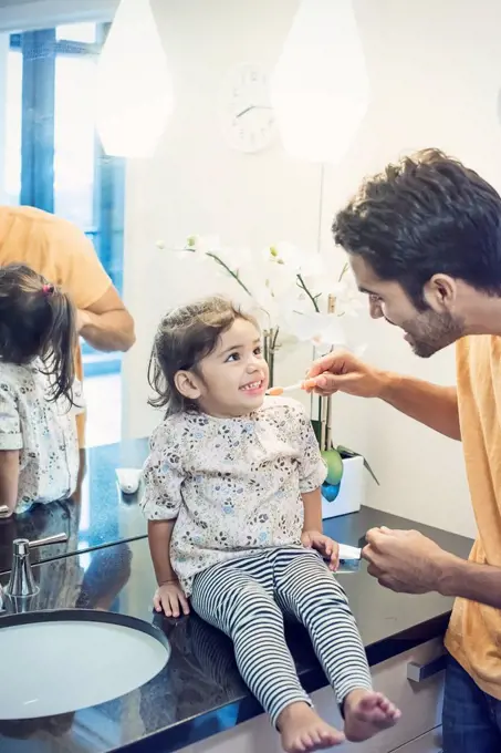 Father and daughter in bathroom brushing teeth