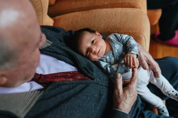 Newborn baby girl on the lap of great grandfather at home