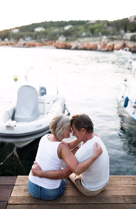 Senior couple sitting head to head on jetty