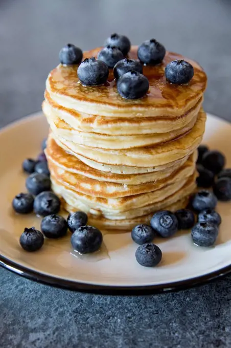 Dish with pile of pancakes and blueberries with maple sirup