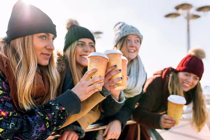 Four friends toasting with coffee to go in winter