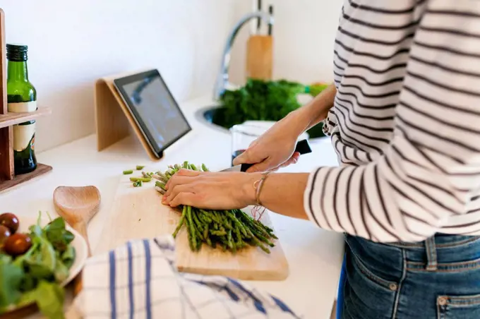 Young woman cooking at home using digital tablet for recipe