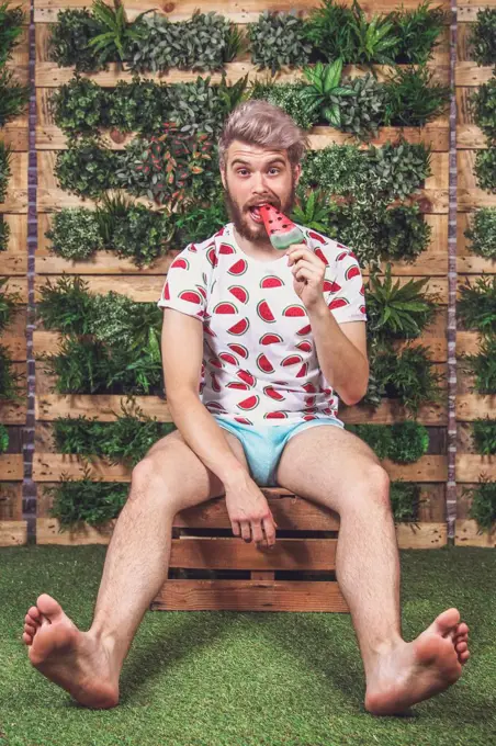 Portrait of young man eating watermelon ice lolly on terrace in front of vertical garden