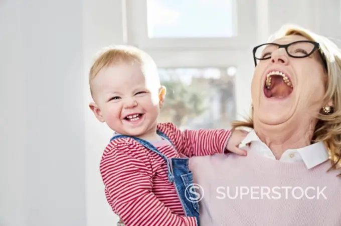 Happy grandmother carrying baby girl at home