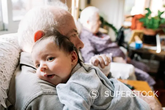 Great-grandfather holding baby at home with his wife in background