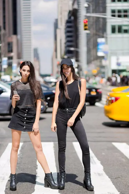 USA, New York City, two fashionable twin sisters standing on zebra crossing in Manhattan
