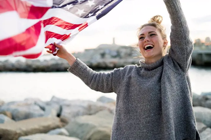 Portrait of laughing young woman holdding blowing US American flag