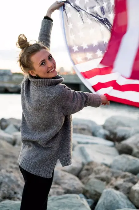 Portrait of smiling young woman holding blowing US American flag