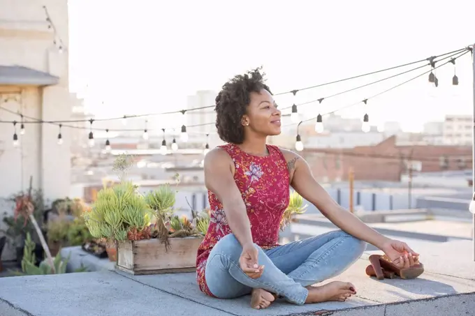 Young woman sitting on rooftop terrace, enjoying the sun