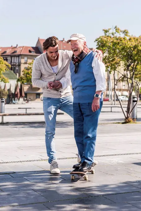 Adult grandson assisting senior man on skateboard