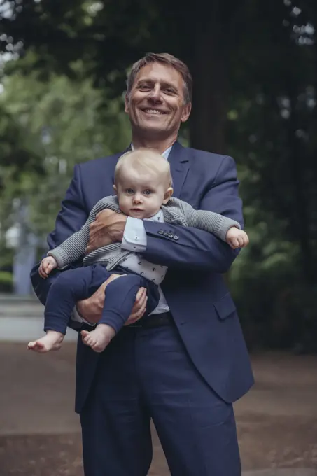 Portrait of smiling mature businessman holding baby boy outdoors