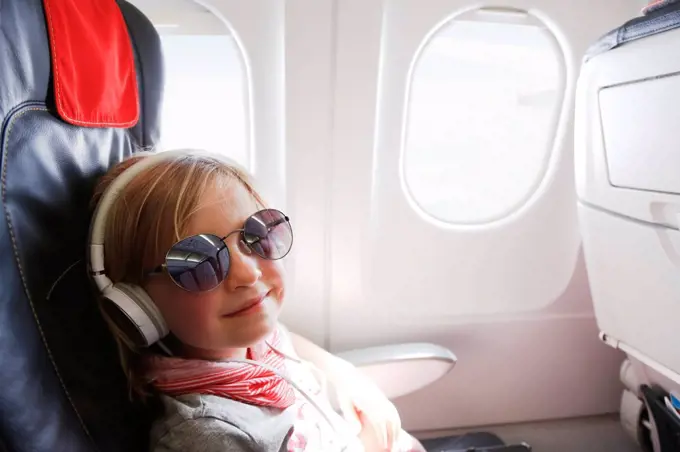 Portrait of smiling little girl with headphones sitting on an airplane