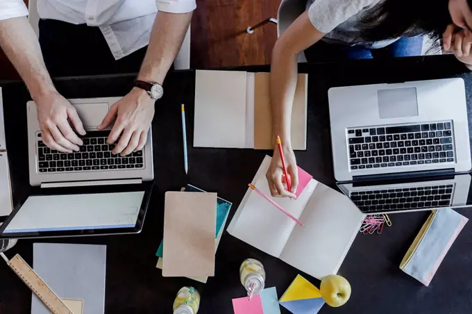 Top view of man and woman using laptops and taking notes