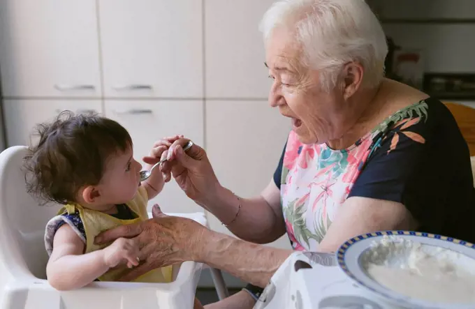 Grandmother feeding baby girl in the kitchen