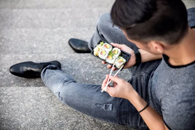 Man sitting on stairs eating takeaway sushi