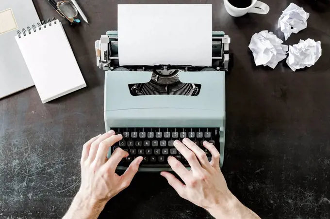 Close-up of man using typewriter with crumpled paper on desk