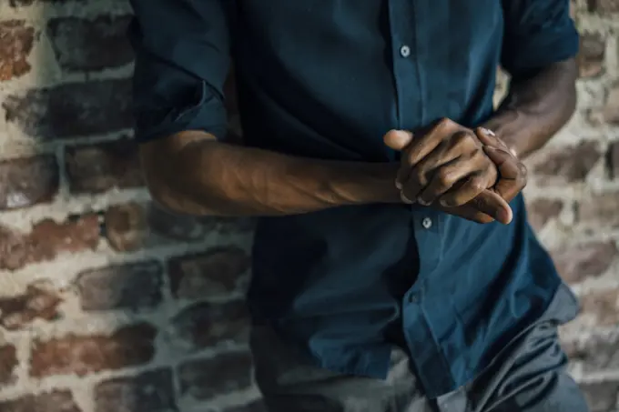 Hands of man leaning against brick wall