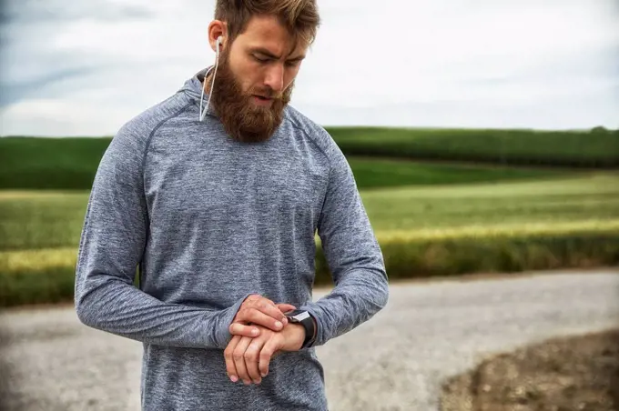 Man with earphones using smartwatch, standing outdoors