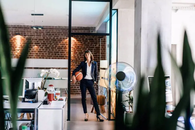 Businesswoman holding basket ball in office