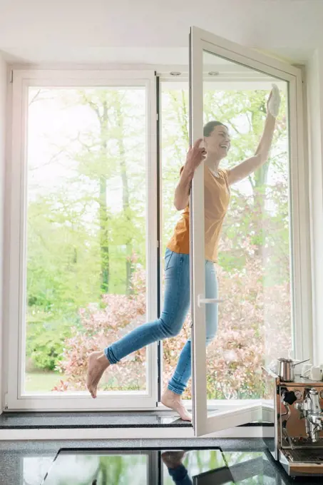 Happy woman standing on windowsill cleaning the window