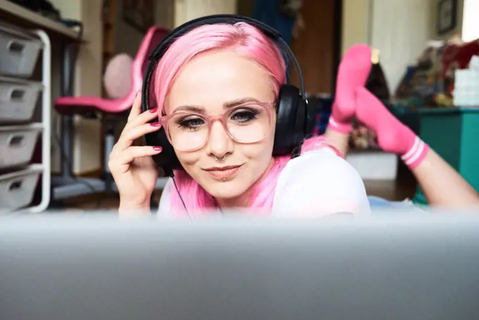 Young woman with pink hair listening to music via laptop at home