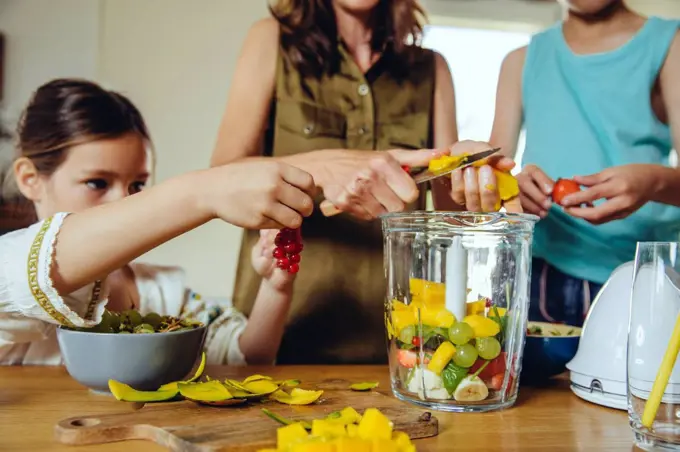 Mother and children putting fruit into a smoothie blender