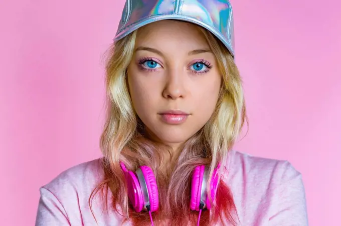 Portrait of young woman with headphones and basecap in front of pink background