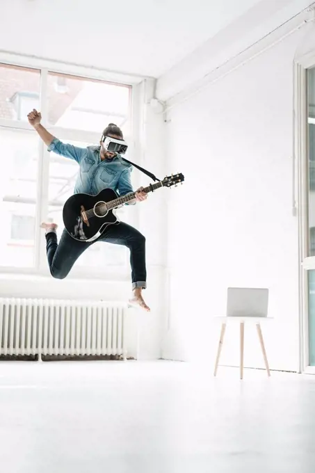 Man with guitar wearing Virtual Reality Glasses jumping in the air in a loft