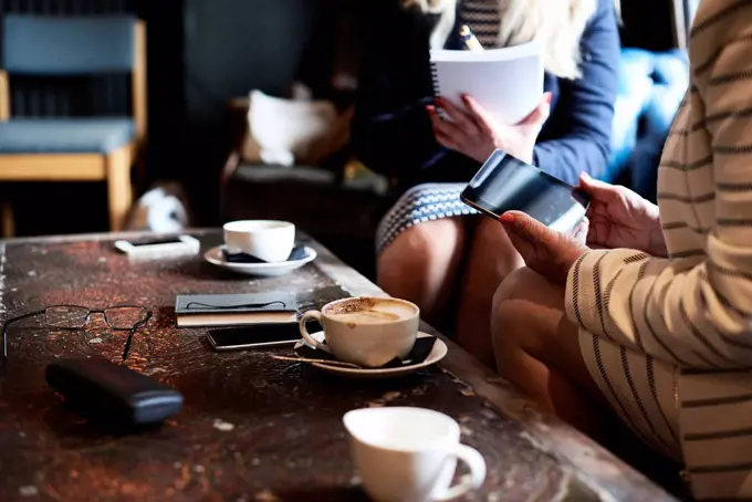 Two businesswomen with tablet and notebook having a meeting at a coffee shop