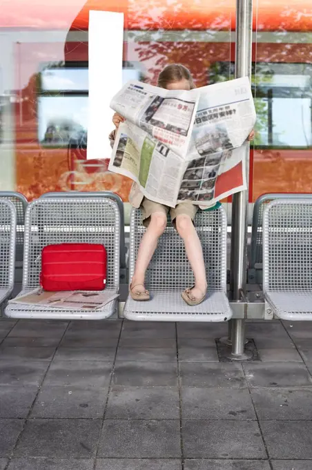 Little girl sitting at platform reading newspaper