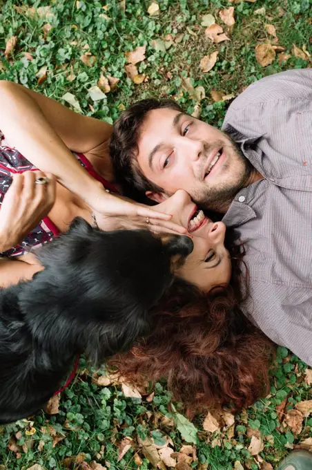 Happy couple in love with dog lying on a meadow