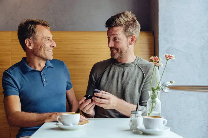 Gay man offering wedding ring to partner in cafe