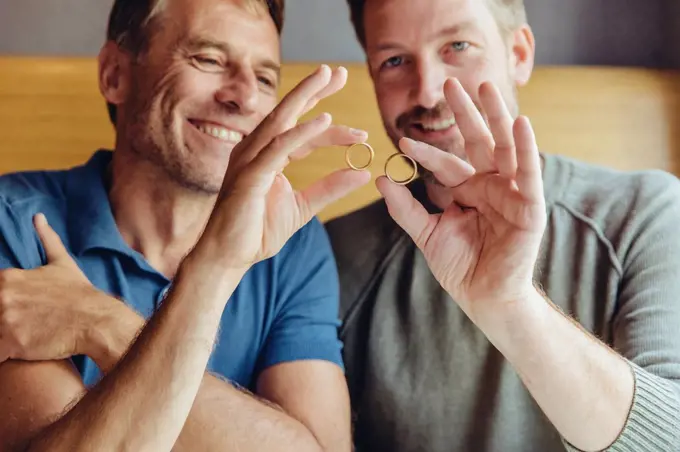 Happy gay couple holding up their wedding rings