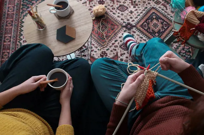 Young couple knitting and having cup of coffee in living room, top view