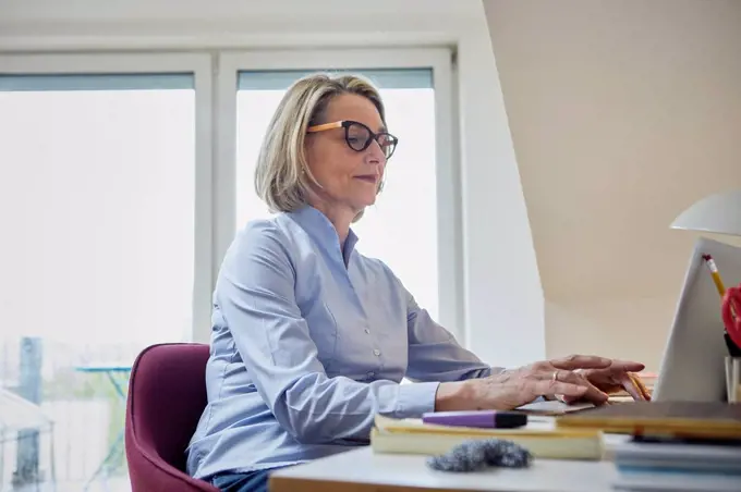 Mature woman at home using laptop at desk