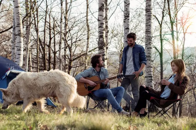 Friends camping in forest with man playing guitar