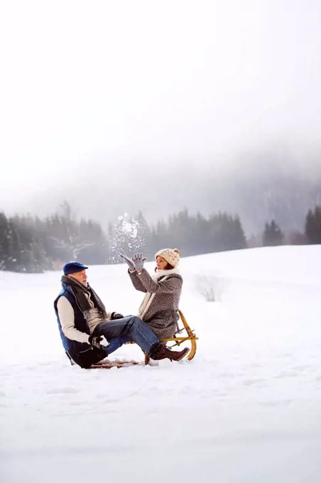 Senior couple with sledge having fun in snow-covered landscape