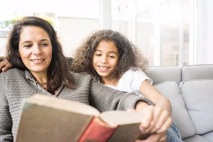 Mother and daughter sitting on couch reading a book