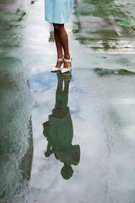 USA, New York, young african-american woman standing on street, high heels, water reflection in puddle