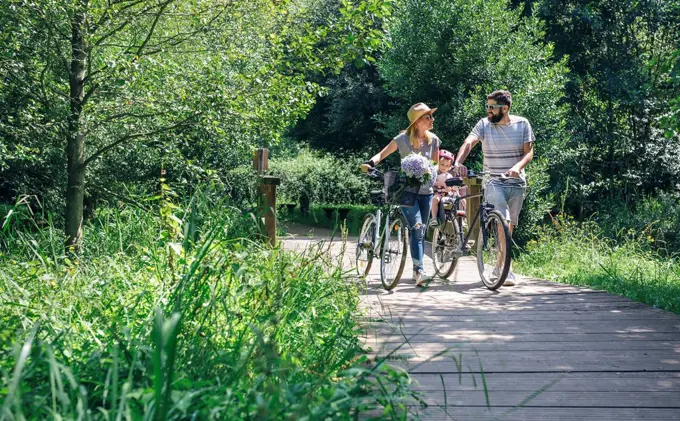 Family pushing bicycles on wooden walkway