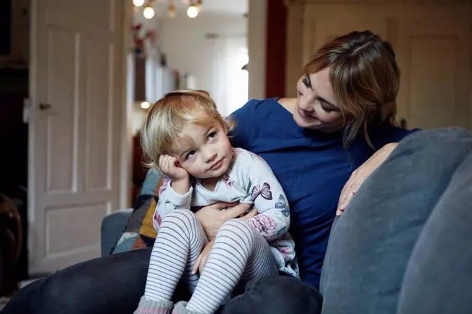 Mother and little daughter sitting together on the couch at home