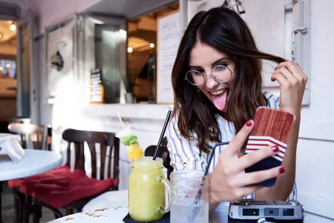 Young woman sitting in a coffee shop taking selfie with smartphone