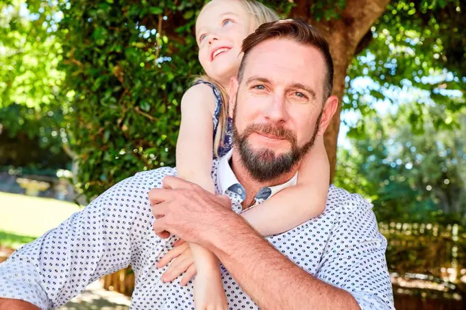 Portrait of smiling father carrying daughter piggyback